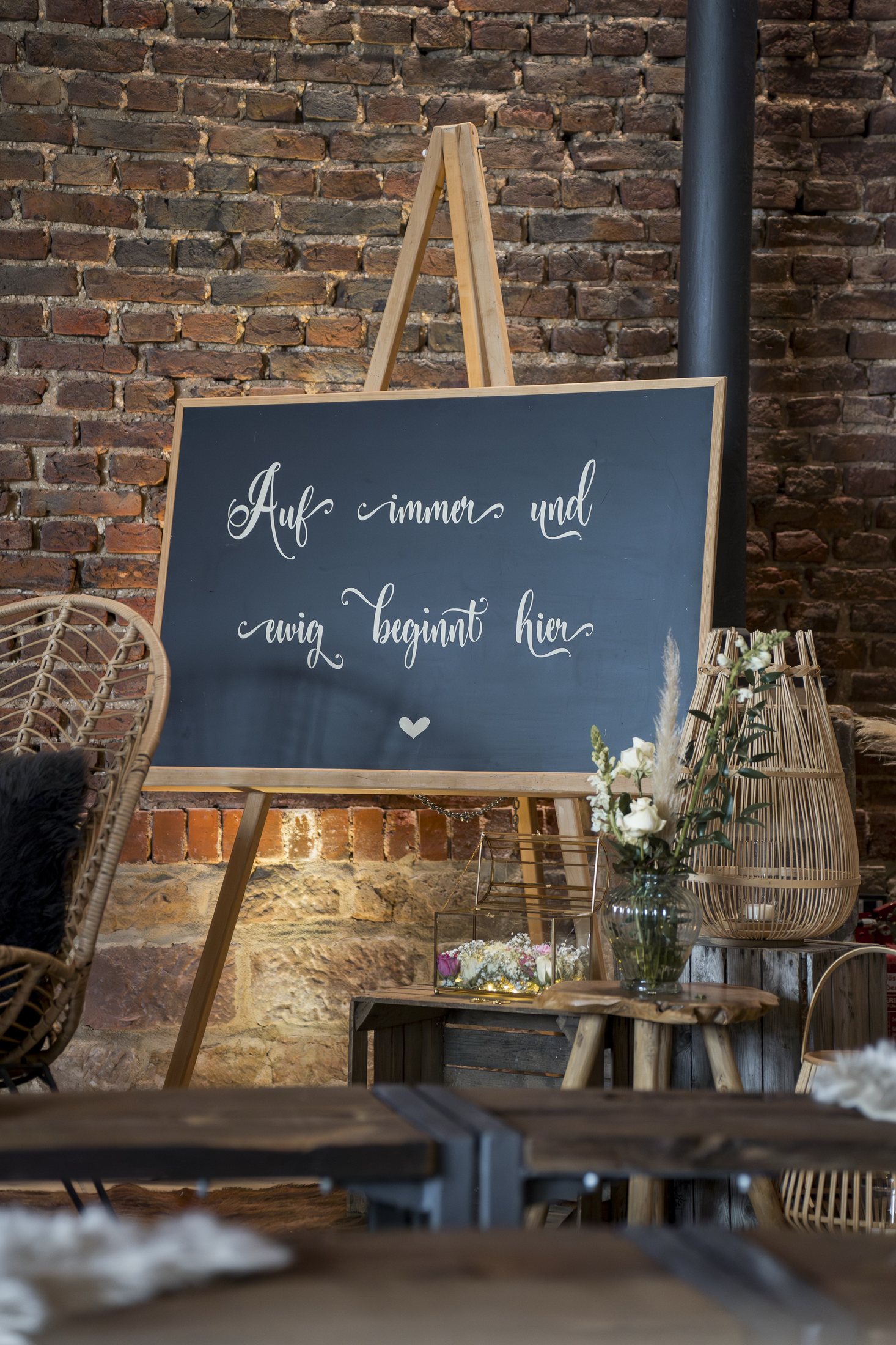 Dekoration für eine Winterhochzeit im Sippelshof Fulda mit Backsteinwand, Kerzen und dem Schild „Auf immer und ewig beginnt hier“